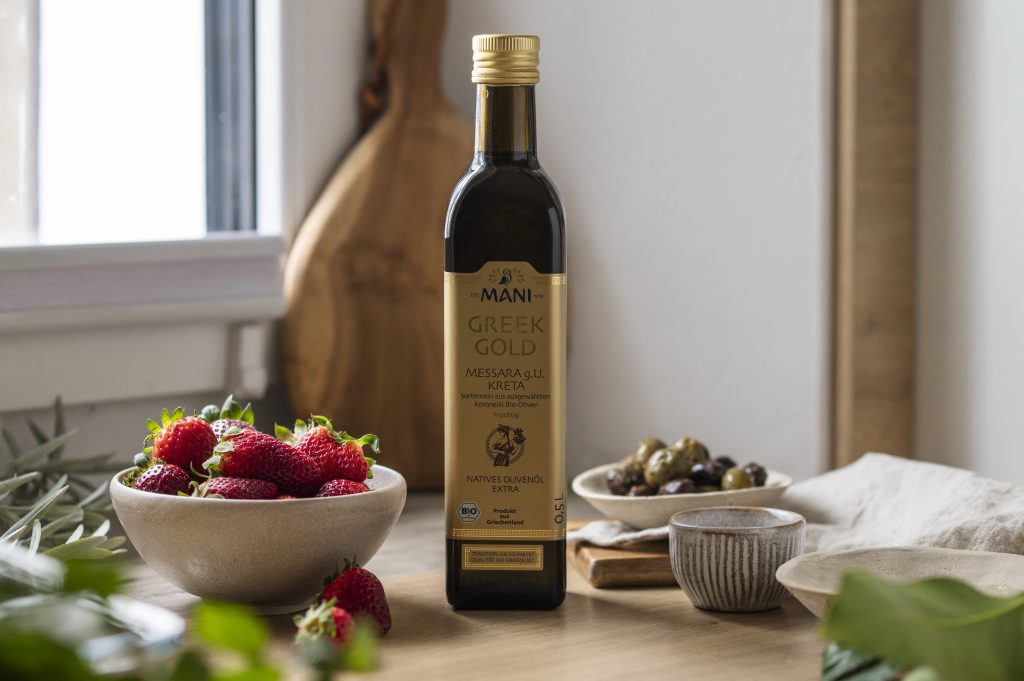 Greek Gold Olivenöl Messara g.U. Kreta in mediterranem Setting mit Schälchen Erdbeeren, Oliven, Öl