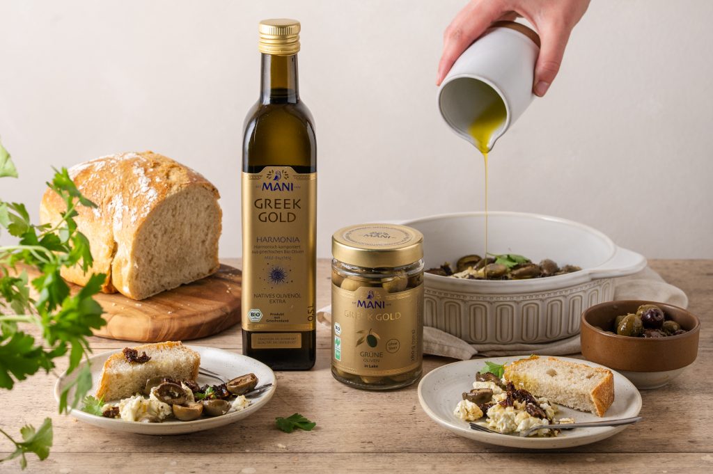 gebackener Feta mit Olivenöl und grünen Oliven auf gedecketem Tisch